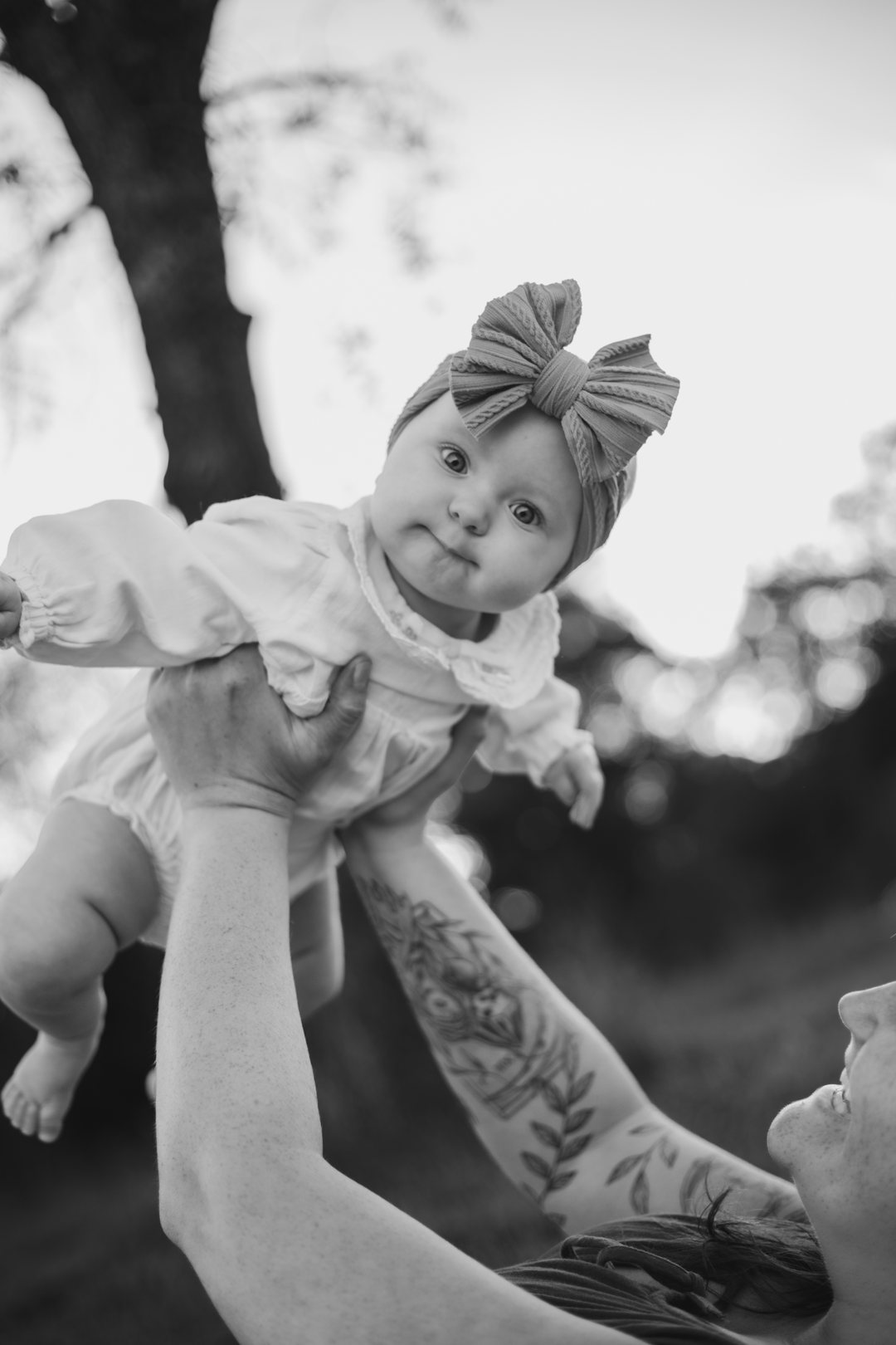 Black and white photo of a baby in a bow headband being lifted into the air