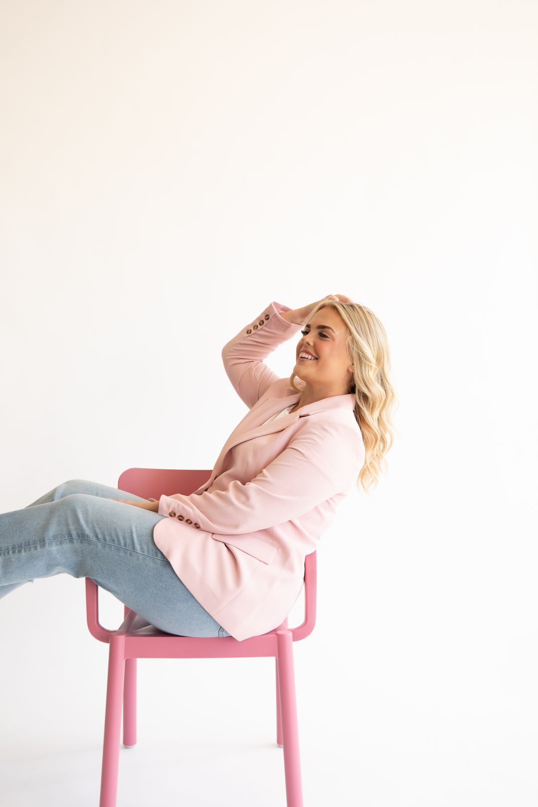 A lash artist in a pink blazer laughing back in a pink chair