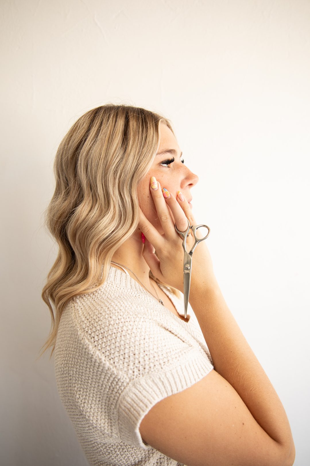 Hair stylist in profile, shears in hand, against a bright white wall