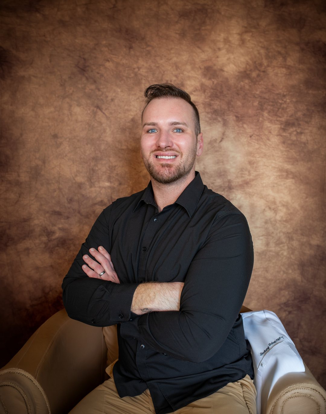 A studio headshot of a man in a black shirt, arms crossed