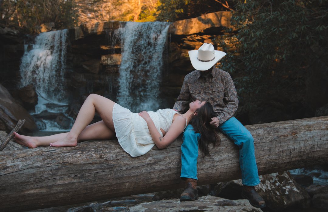 A couple resting together on a fallen log in front of a waterfall at golden hour
