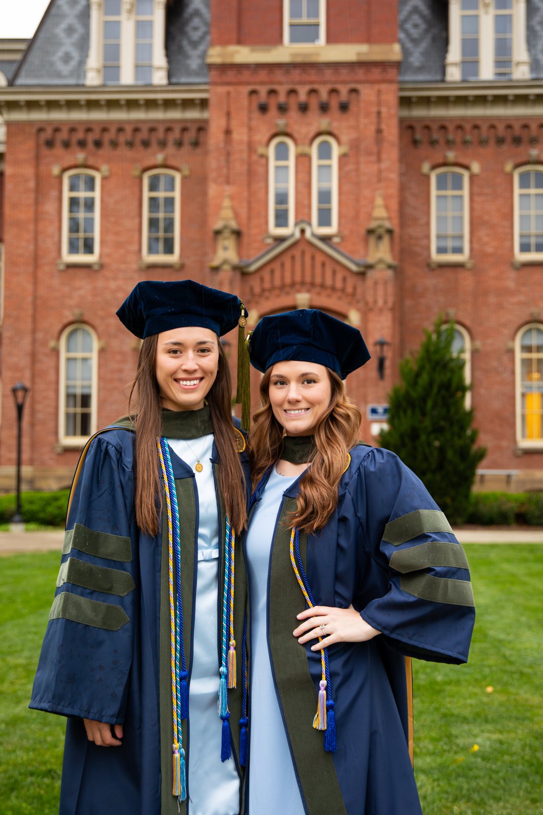 Two graduates in doctoral robes and caps in front of Woodburn Hall