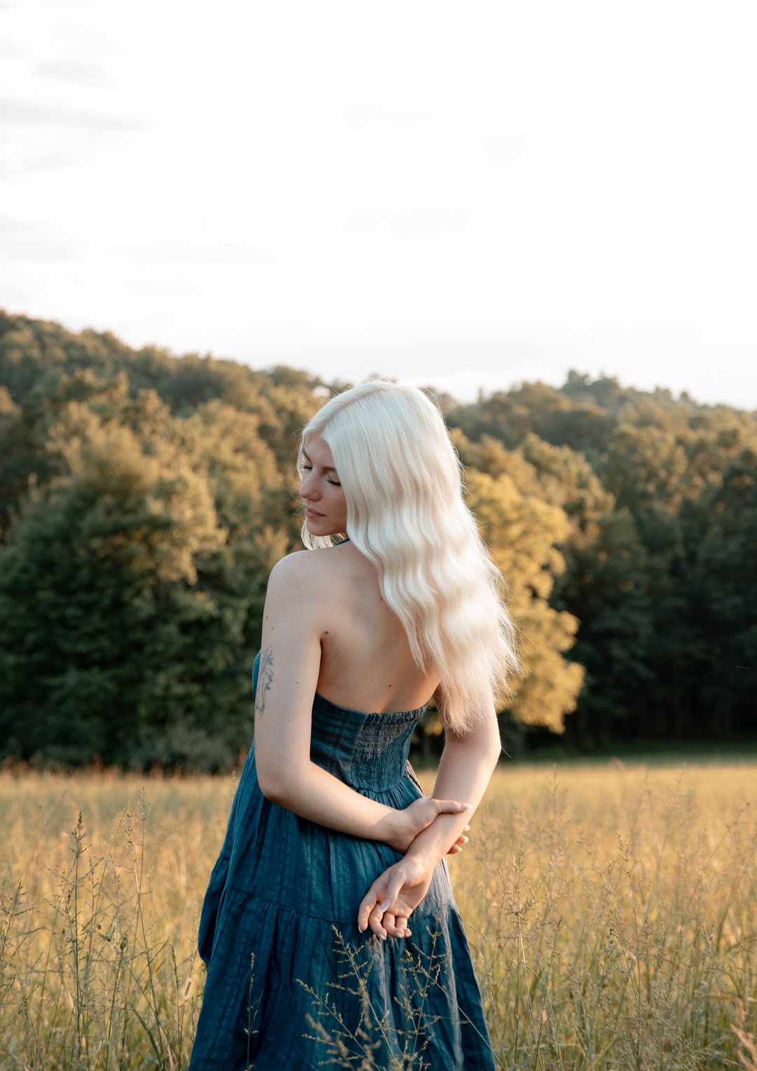 A senior in a blue dress looking over her shoulder in a sunlit field