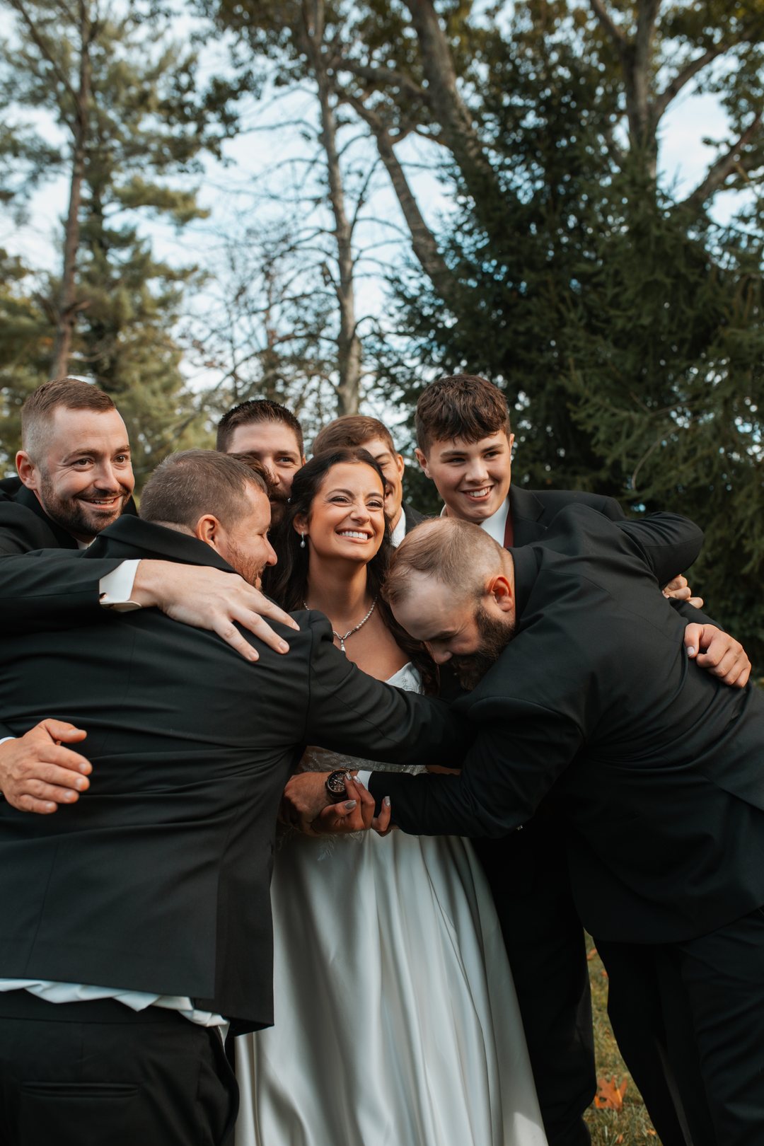 A bride laughing in the middle of a group hug with the wedding party